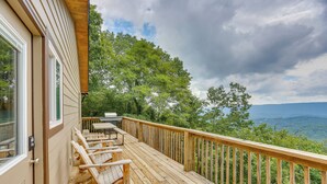 A wooden deck with outdoor furniture, a view of trees and mountains, and a wooden railing.