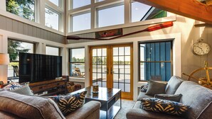 A spacious living room with a large TV, comfortable seating, and a view of the outdoors through large windows. - Gorgeous Long Lake Home w/ Dock, Kayak, SUP & More (Lacey)