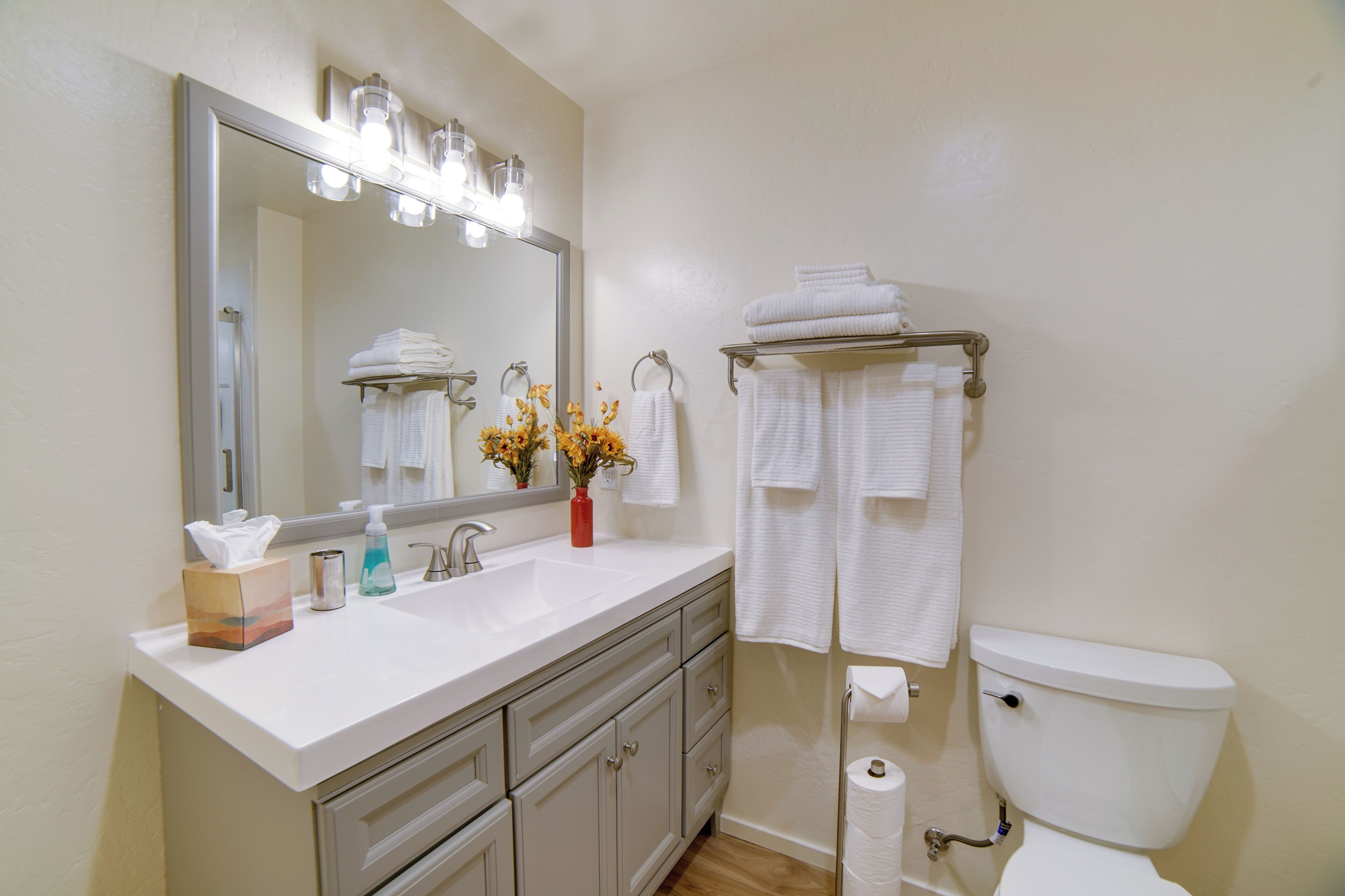 A bathroom with a white sink, mirror, and toilet. There are towels on a rack and a vase with flowers on the sink.
