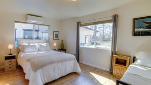 Un dormitorio con una cama grande, una mesita de noche, una ventana con cortinas y un cuadro enmarcado en la pared.