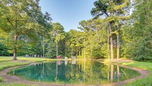Un étang paisible, entouré de grands arbres et bordé d’un petit abri, au cœur d’un parc verdoyant.
