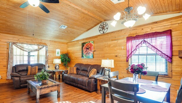 L’intérieur d’un chalet confortable, avec un plancher en bois, un canapé en cuir, une table à manger et un ventilateur de plafond.