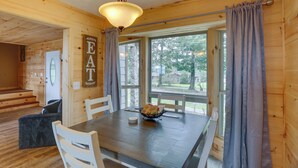 L’intérieur d’un chalet en bois, avec une table à manger, des chaises, un lustre et une vue par les fenêtres.