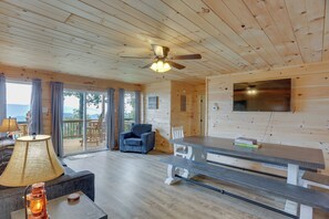 A wooden cabin interior with a ceiling fan, a dining table, a sofa, and a TV mounted on the wall. - Mtn-view Gem: Flat Rock Retreat w/ Deck & Grill! (Flat Rock)