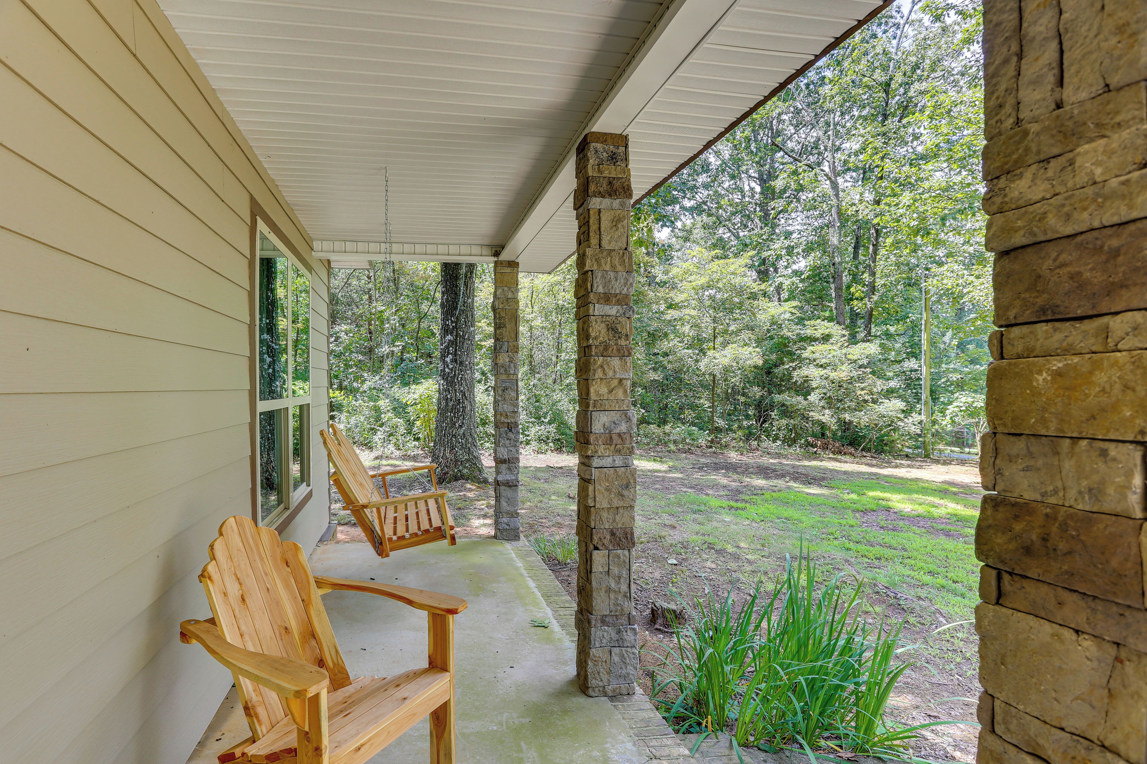 Eine überdachte Veranda mit zwei Holz-Adirondack-Stühlen und einer Steinpfeiler.