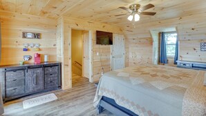 Une chambre dans une cabane en bois, avec un lit, une commode, un ventilateur de plafond et une fenêtre.
