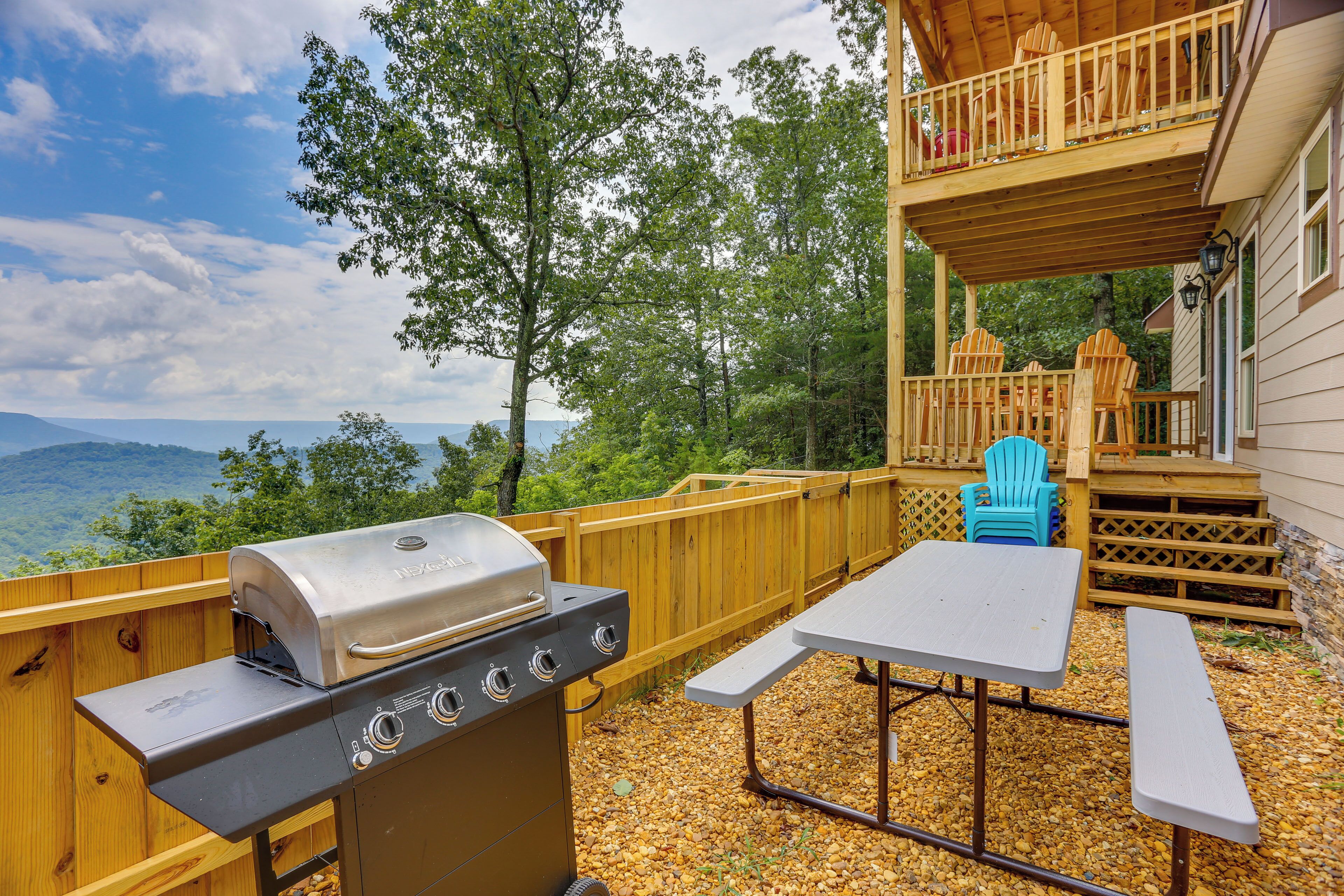 A wooden deck with a grill, a picnic table, and Adirondack chairs.