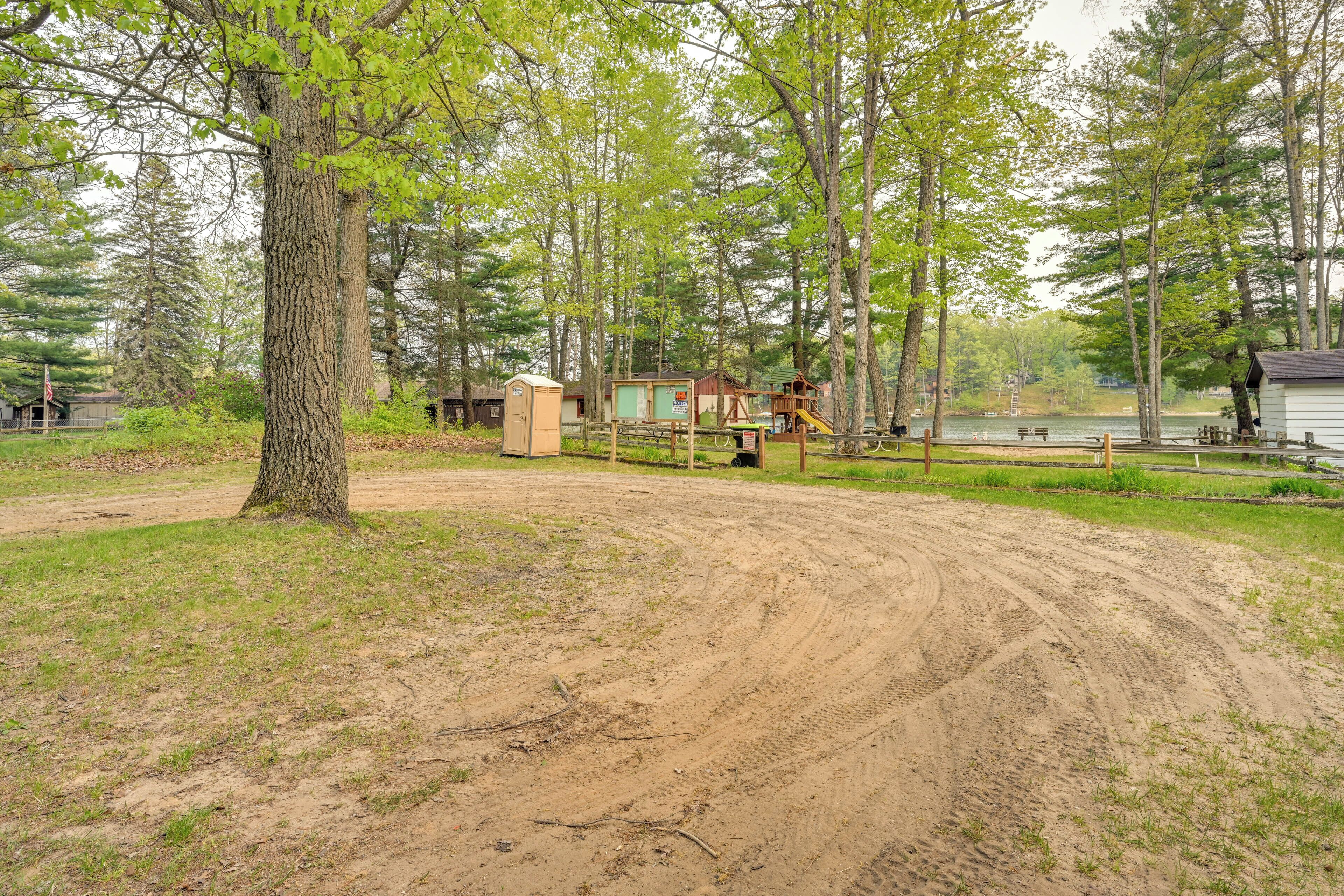 A dirt path leading to a wooden structure with a small building and a swing set.
