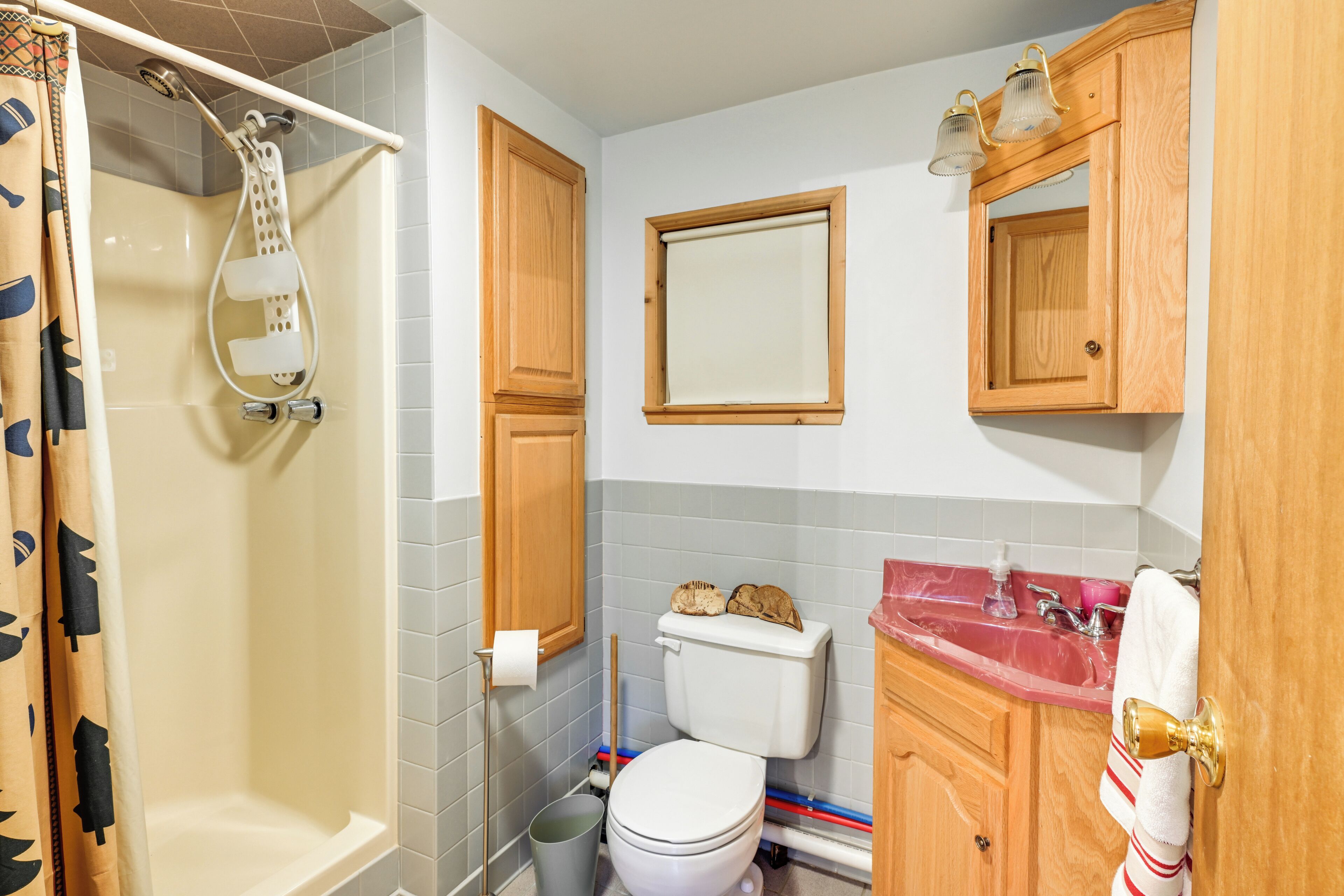 A bathroom with a shower, toilet, sink, and wooden cabinets.