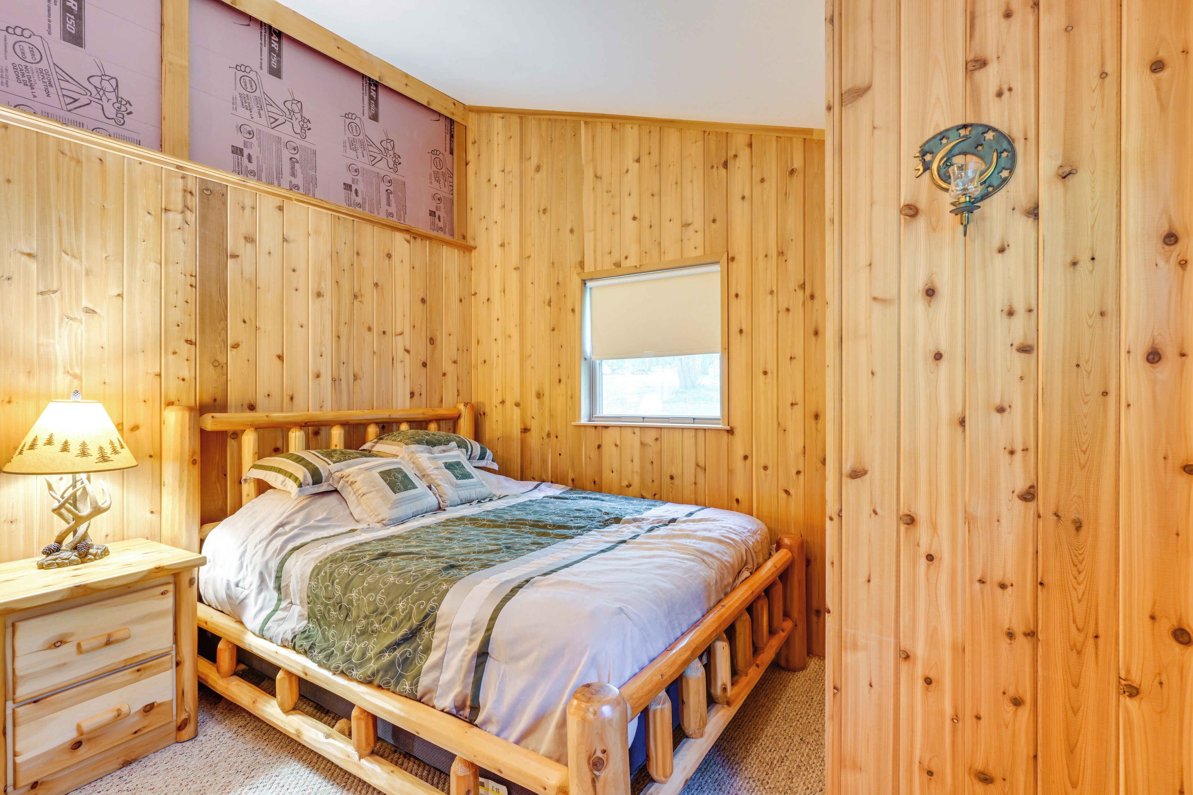 A wooden-paneled bedroom with a bed, a nightstand, and a window.