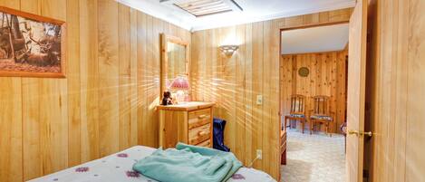 A wooden-paneled bedroom with a bed, a dresser, a mirror, and a painting of deer.