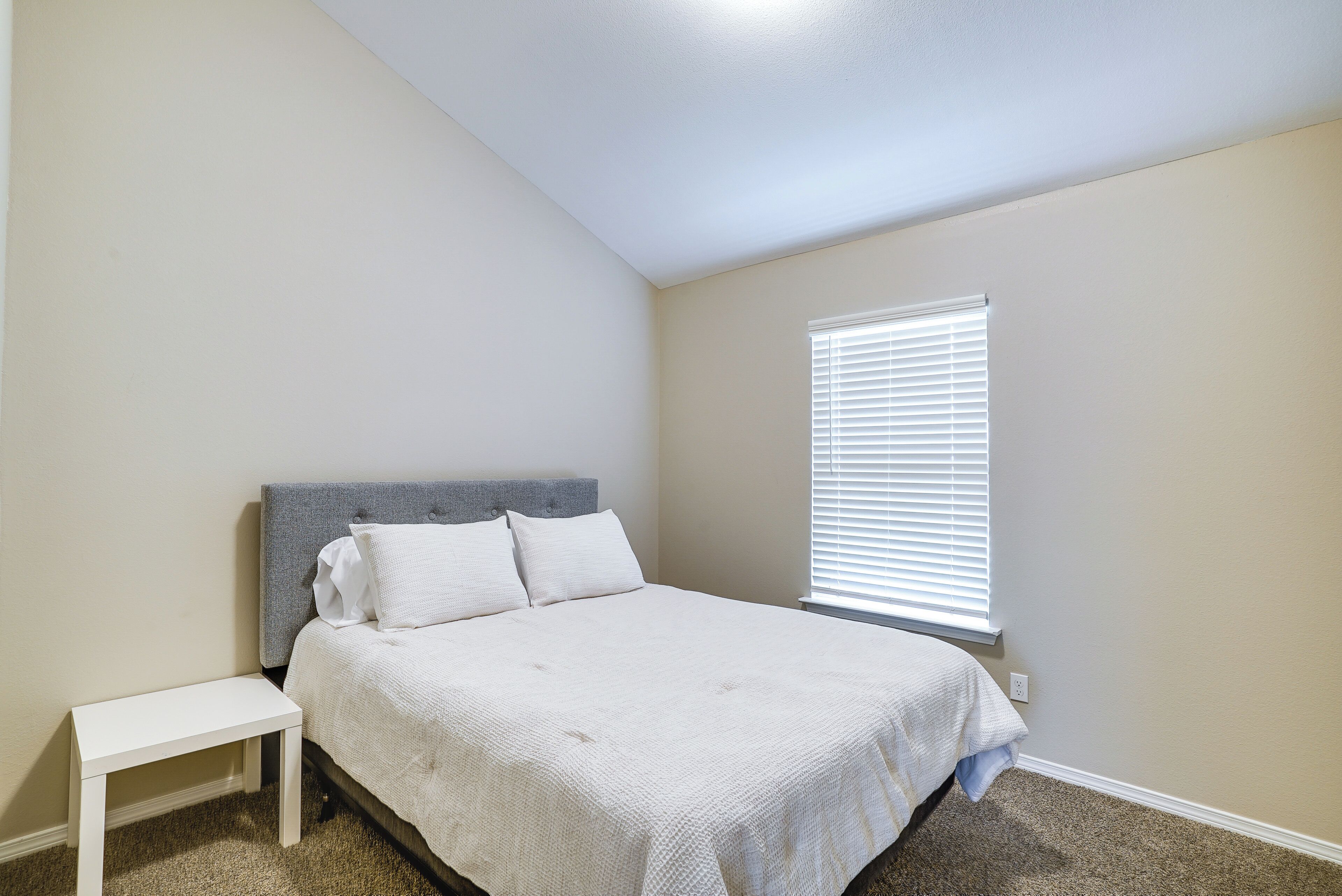 A bedroom with a bed, a nightstand, and a window with blinds.