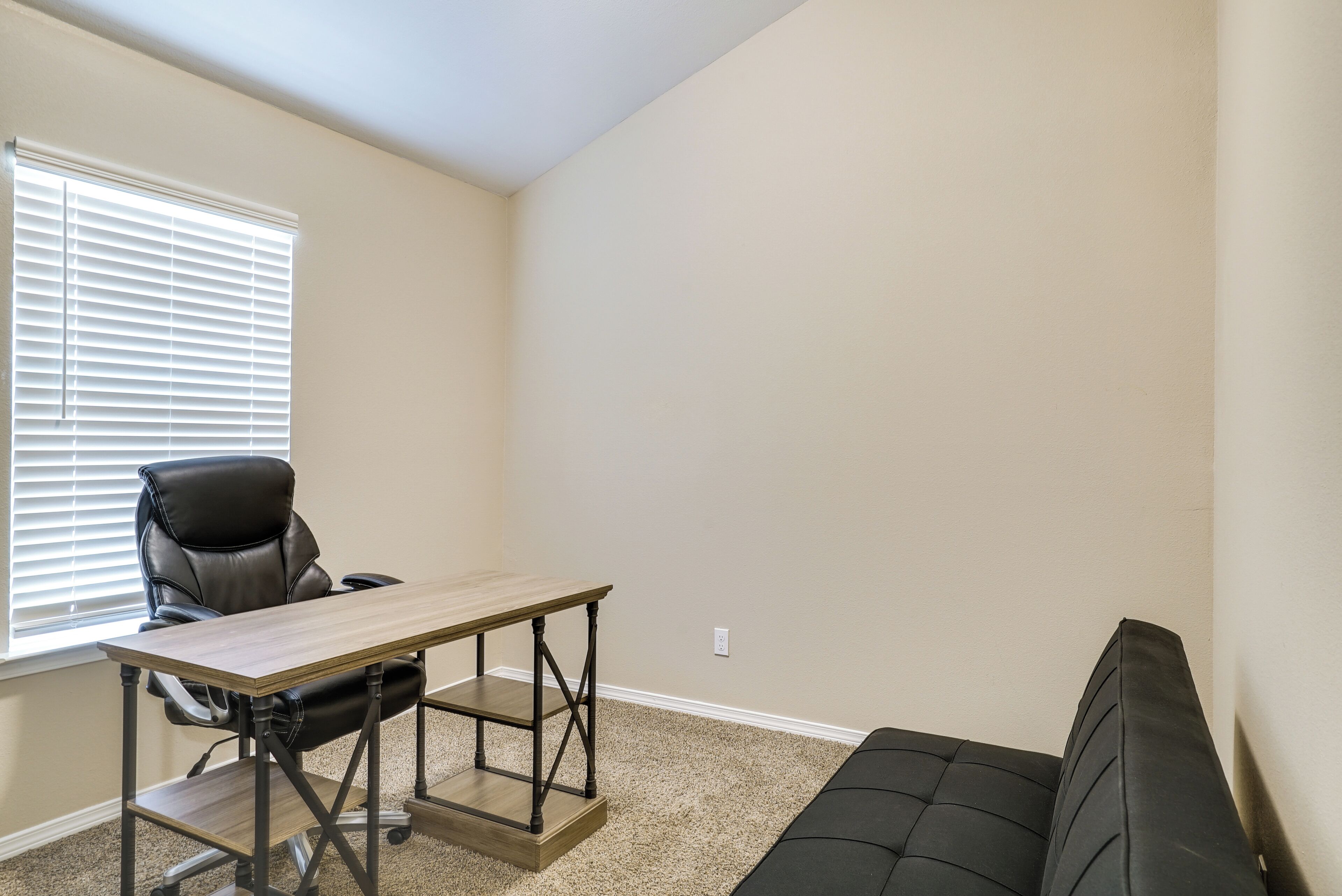 Une pièce comprenant un fauteuil en cuir noir, un bureau en bois et un canapé noir.