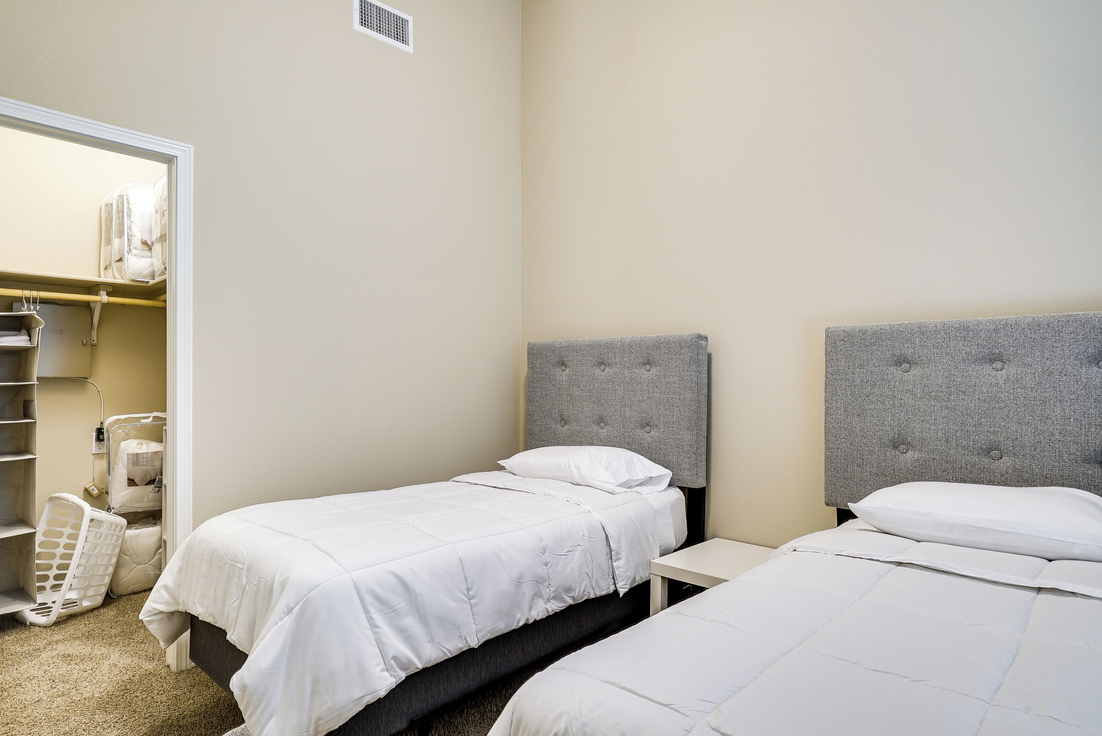 A bedroom with two beds, a bedside table, and a closet with hanging clothes.