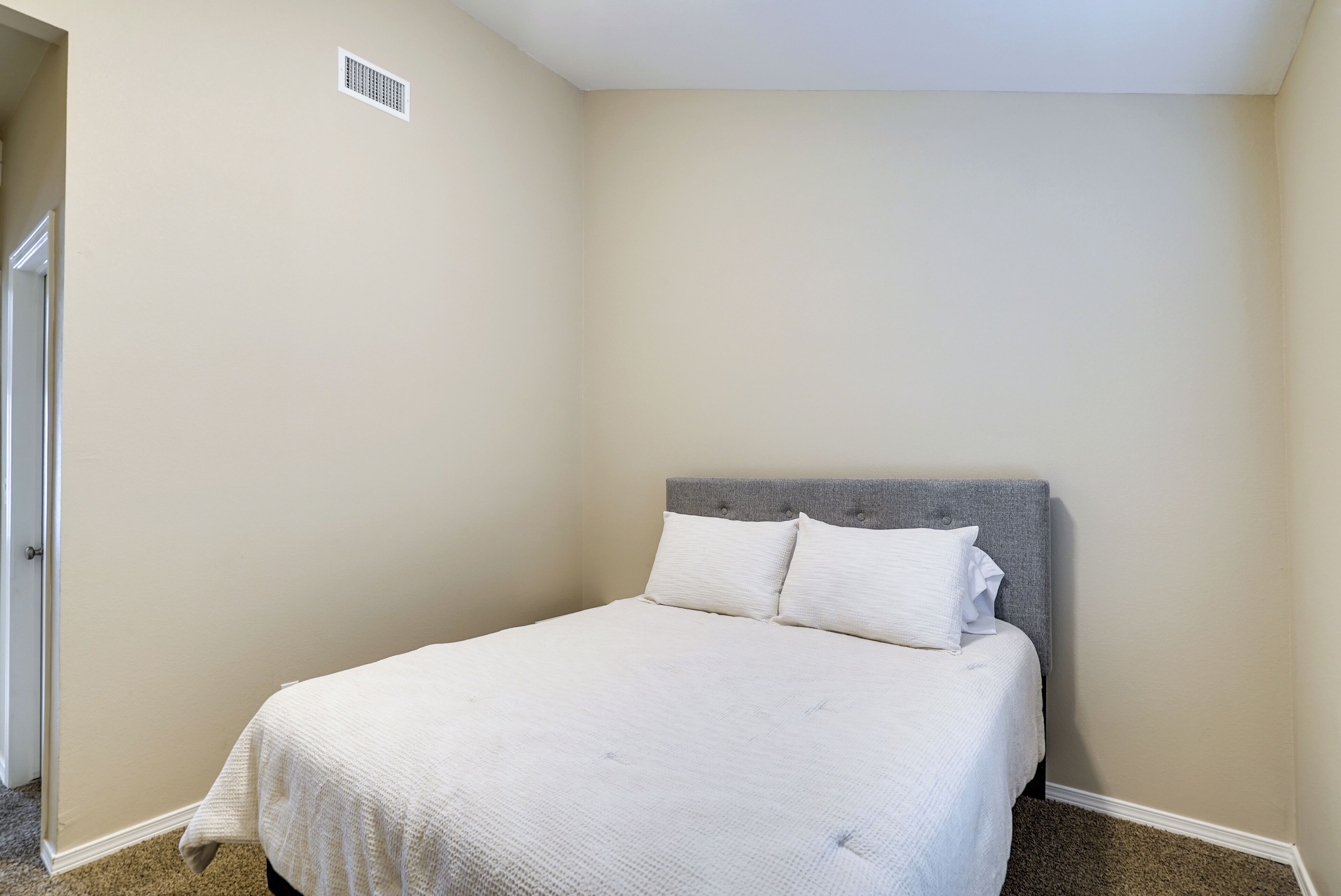 A bedroom with a single bed, a grey headboard, and beige walls.