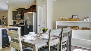 Una cocina moderna con armarios de madera oscura, un refrigerador de acero inoxidable y un comedor con mesa y sillas de madera.