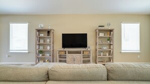 Una sala de estar con un televisor de pantalla plana grande sobre un mueble de madera, flanqueado por dos estanterías con objetos decorativos.