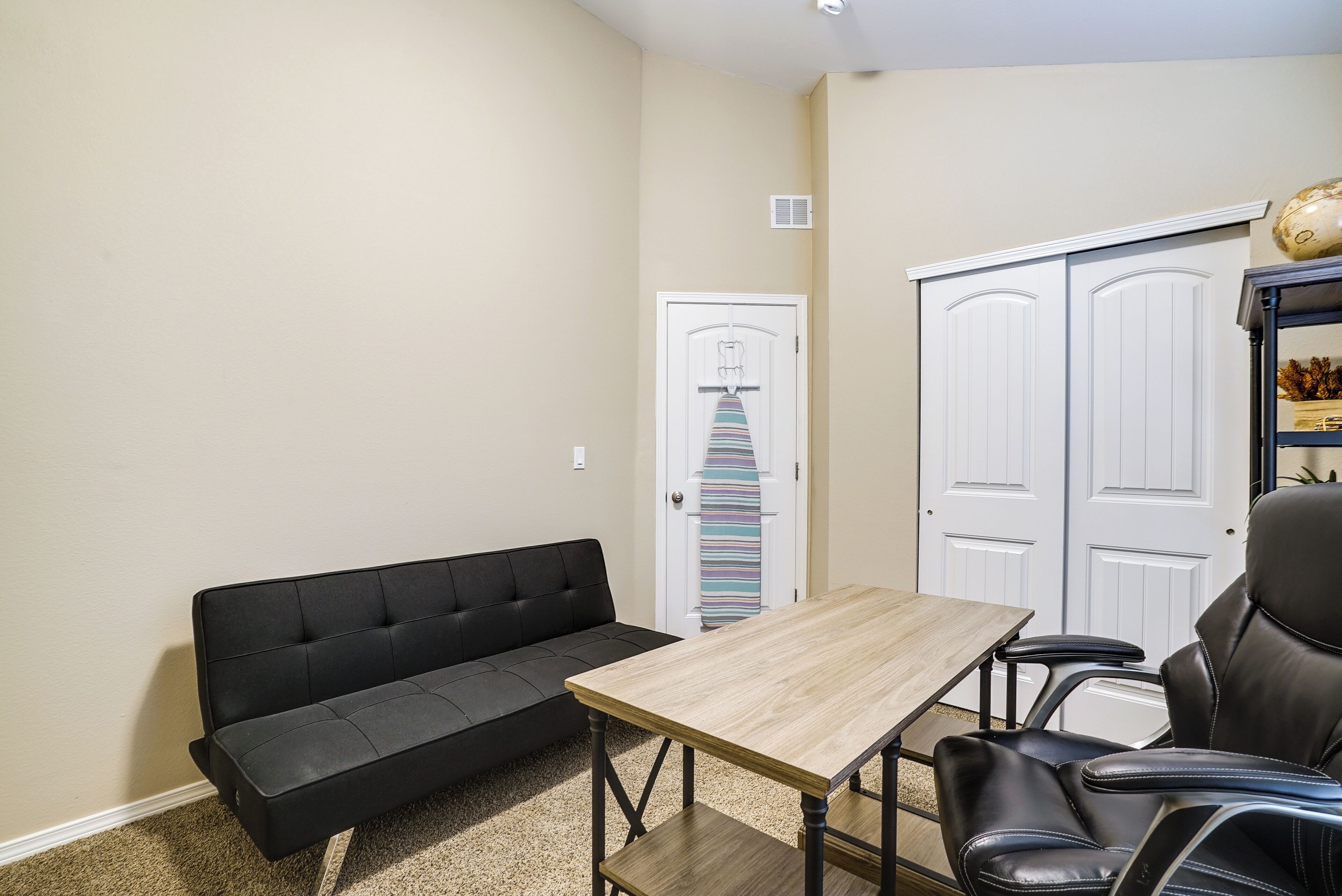 A room with a black sofa, a wooden table, and a black leather chair.