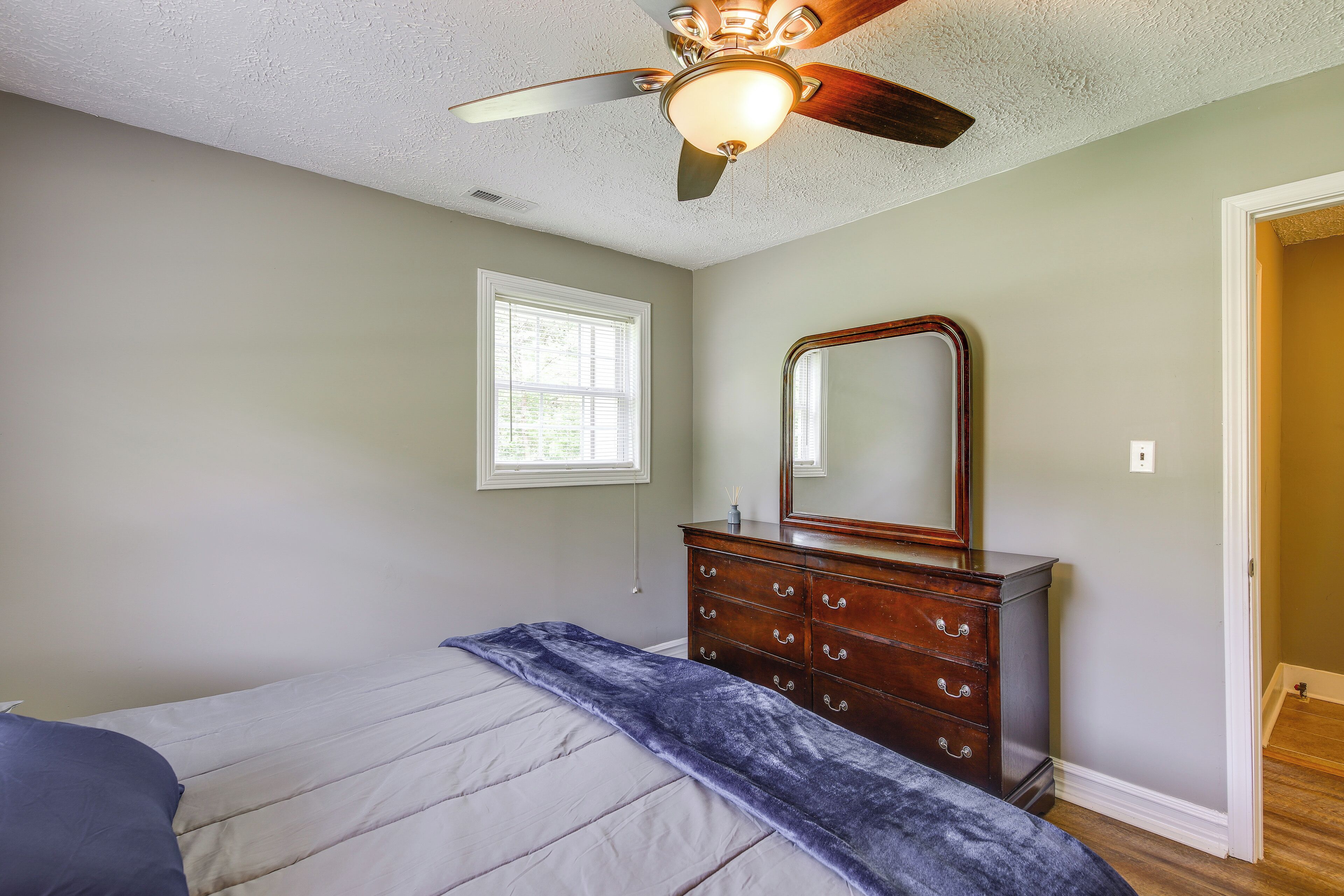 Une chambre à coucher avec un lit, une commode, un ventilateur de plafond et une fenêtre.