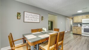 Un coin repas avec une table dressée pour six personnes, entourée de chaises en bois. Un cadre contenant une citation est accroché au mur, au-dessus de la table.