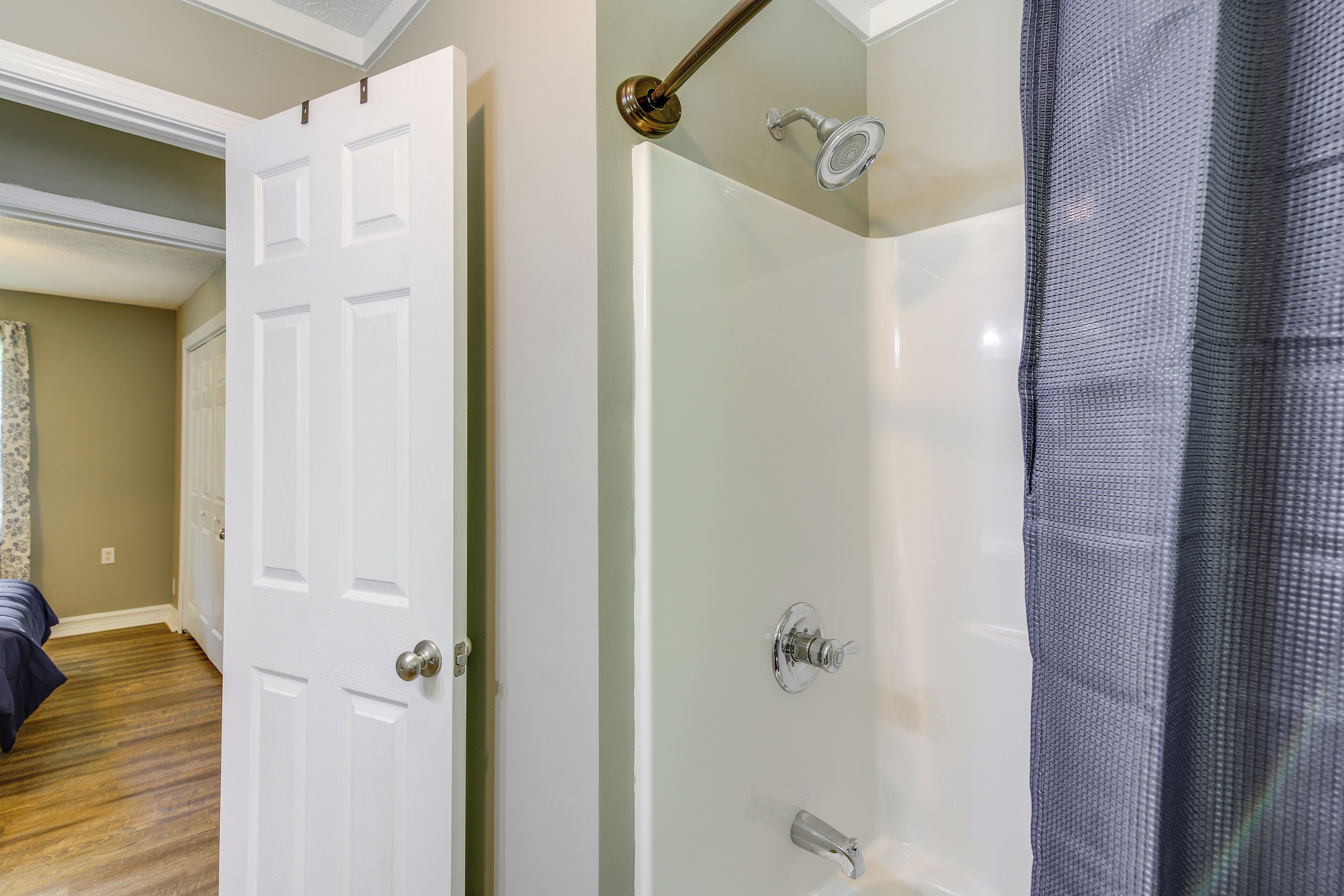 A bathroom with a white door, a shower with a glass enclosure, and a grey shower curtain.