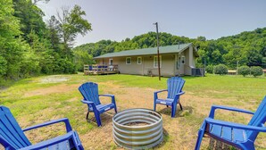 Une maison avec un toit végétalisé, entourée d’une cour verdoyante où se trouvent deux chaises Adirondack bleues et un foyer en métal.