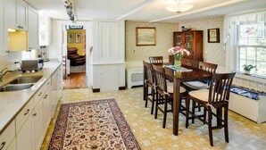 Une cuisine avec coin repas, dotée d’un sol carrelé, de meubles en bois, d’un tapis et d’une table à manger avec des chaises.