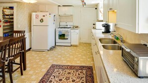 Une cuisine compacte équipée d’un réfrigérateur, d’une cuisinière, d’un four à micro-ondes et d’un grille-pain. On y trouve une table à manger avec des chaises et un tapis à motifs.