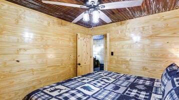A wooden room with a bed, a ceiling fan, and a door leading to another room.