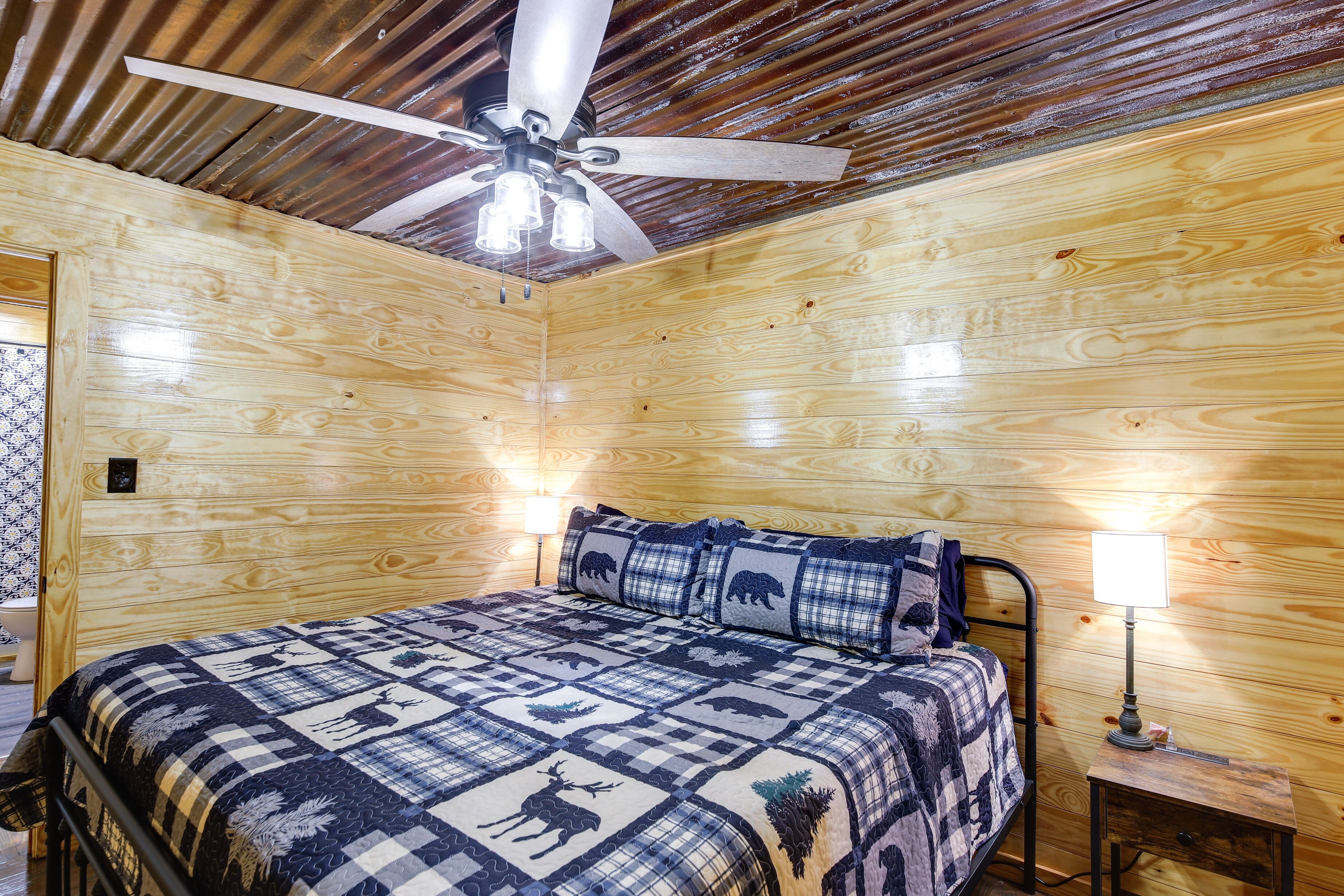 Ein Zimmer in einer Holzhütte mit einem Bett, einem Deckenventilator und einem Nachttisch mit Lampe.