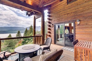 Une terrasse en bois avec une table ronde et des chaises, offrant une vue sur un lac et des montagnes.