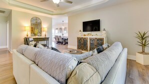 A living room with a large sofa, a ceiling fan, a television, and a dining area in the background. - Russellville Home Near Hiking + Lake Access! (Russellville)