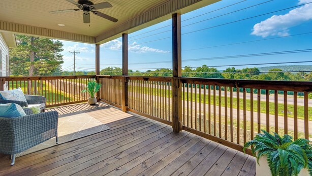 A wooden deck with a ceiling fan, outdoor furniture, and a view of a road and greenery. - Russellville Home Near Hiking + Lake Access! (Russellville)