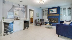 A modern living room with a blue sofa, a fireplace, and a kitchen area with a built-in oven. - Ponte Vedra Beach Vacation Rental w/ Private Pool! (Ponte Vedra Beach)