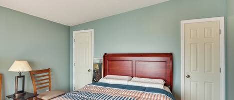 A bedroom with a bed, a nightstand, a lamp, a chair, and a door.