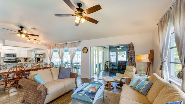 A spacious living area with a large sofa, a coffee table, and a dining table with chairs. There are ceiling fans and a kitchen in the background. - Breezy Englewood Condo w/ Community Pool! (Englewood)