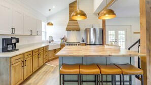 Une cuisine moderne avec des meubles en bois, un grand îlot central doté de tabourets, des appareils en acier inoxydable et un éclairage suspendu.