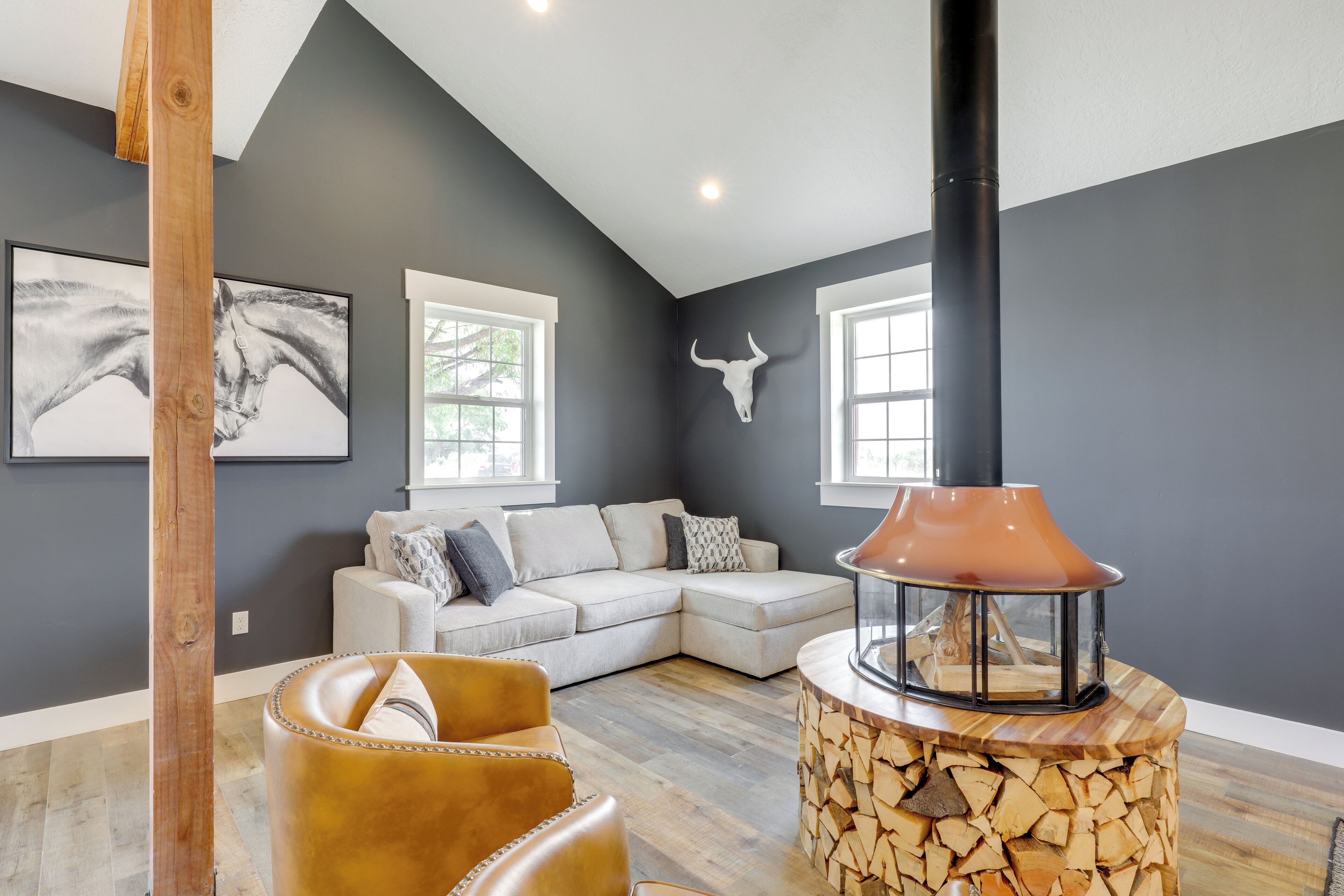 Un salon moderne avec un canapé d’angle, un fauteuil en cuir, un poêle à bois et des œuvres d’art accrochées aux murs.