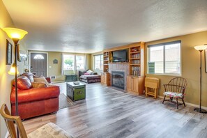 A spacious living room with a fireplace, a leather sofa, a wooden bookshelf, and a television. - Winchester Bay Vacation Rental Near Dunes & Atv! (Reedsport)