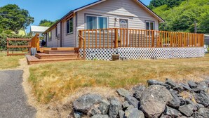 A single-story house with a wooden deck and a stone wall in front. - Winchester Bay Vacation Rental Near Dunes & Atv! (Reedsport)