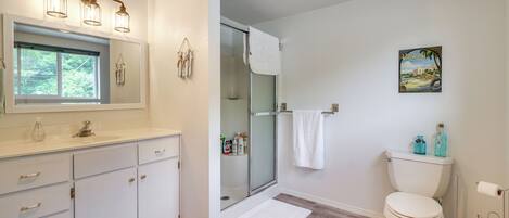 A bathroom with a white vanity, a glass shower enclosure, a toilet, and a framed picture on the wall.