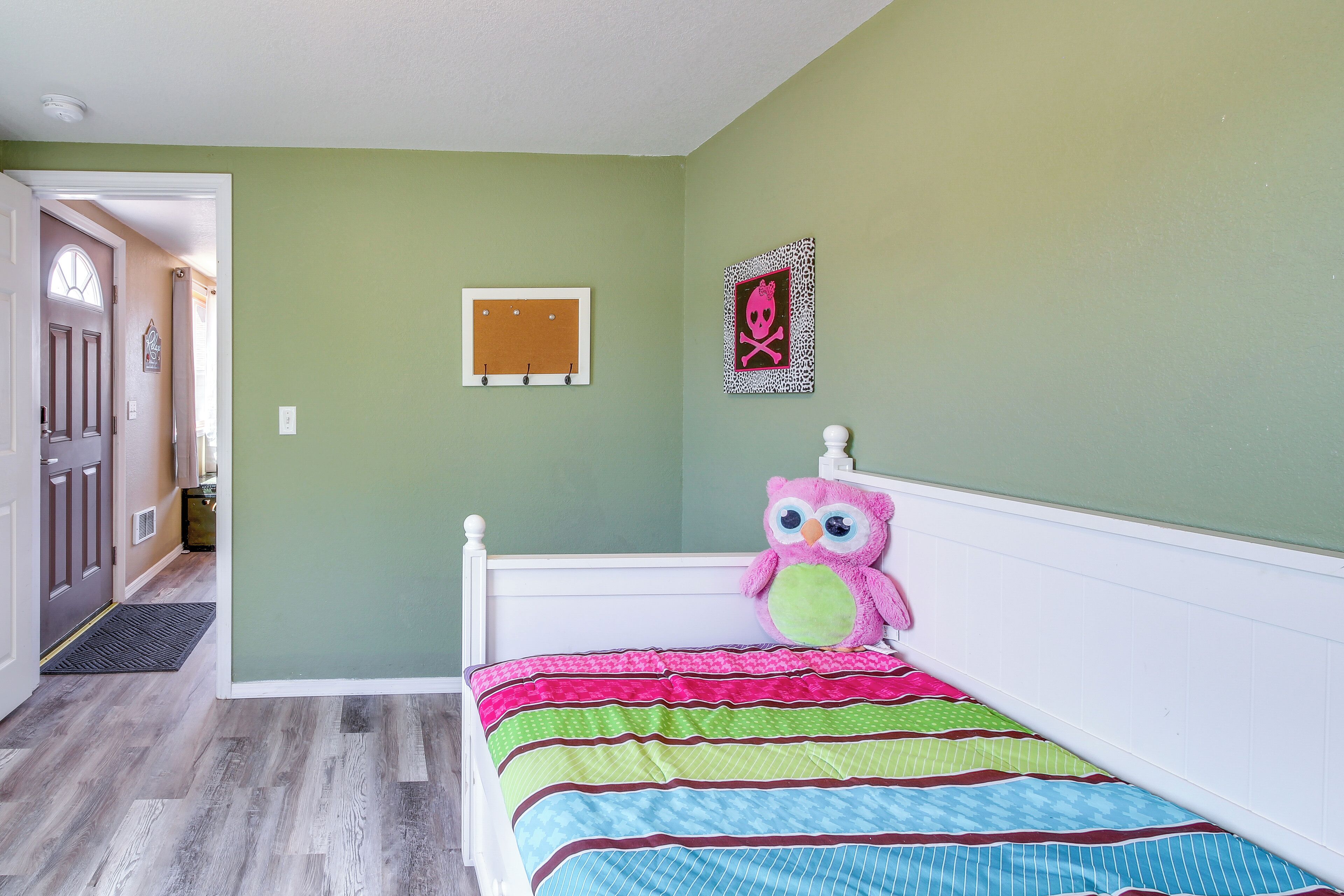 Une chambre à coucher comprenant un lit, une porte, un tableau d’affichage mural en liège et un décor encadré représentant un crâne et des os croisés.