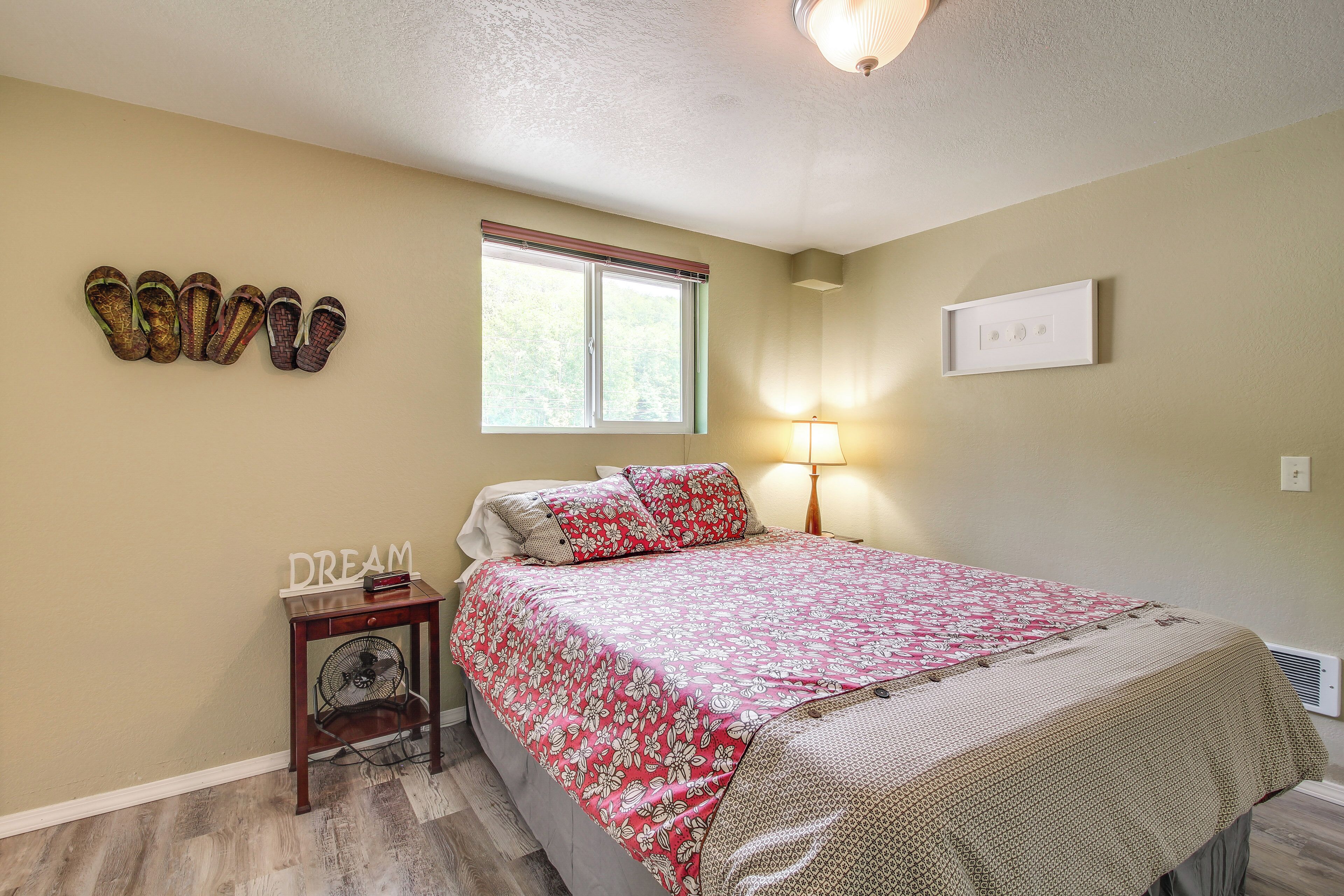 Un dormitorio con cama, mesita de noche, lámpara, ventana y aire acondicionado instalado en la pared.