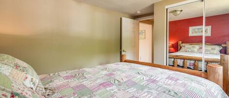 A bedroom with a bed, a mirror, and a door leading to another room.