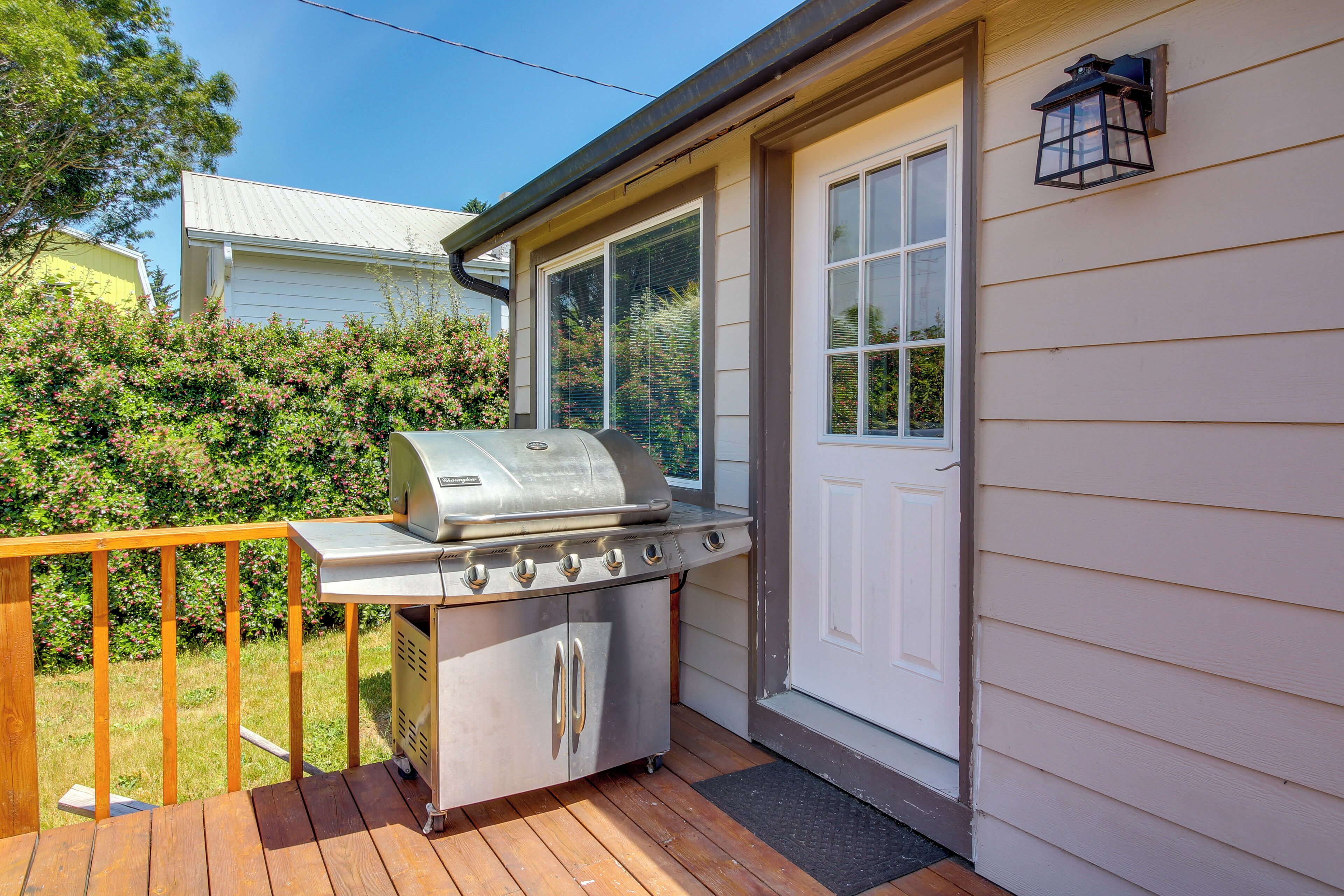 Una parrilla para barbacoa en una terraza de madera, una puerta blanca y una ventana con vistas a follaje.
