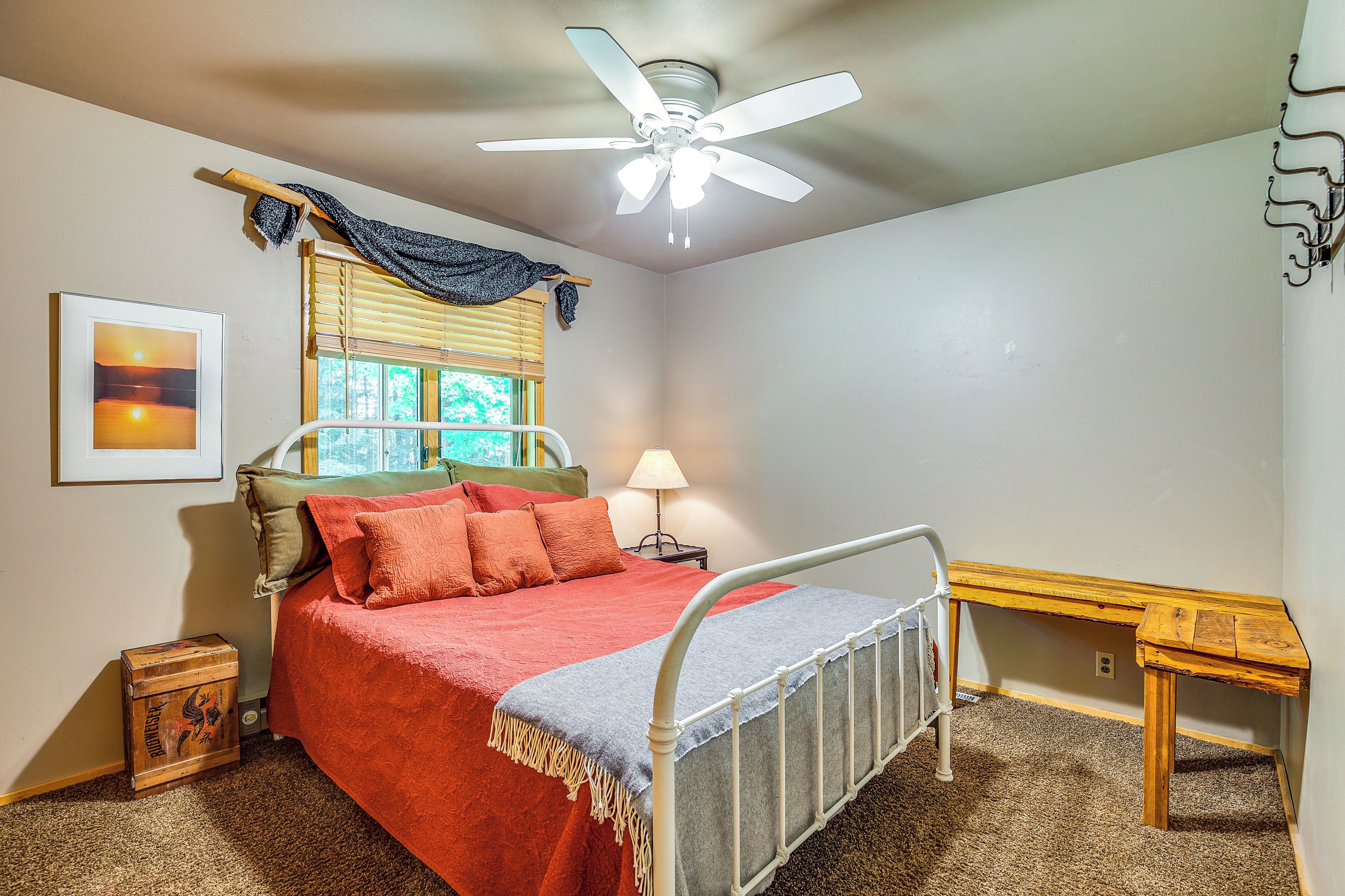 A bedroom with a bed, a ceiling fan, a window with blinds, a bedside table, and a lamp.