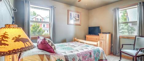 A bedroom with a bed, a desk, a chair, a ceiling fan, and a window with curtains.