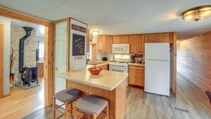 A kitchen with wooden cabinets, a central island with stools, a stove, a microwave, and a refrigerator. - Lakefront Wisconsin Home w/ Boat Dock & Fire Pit! (Townsend)