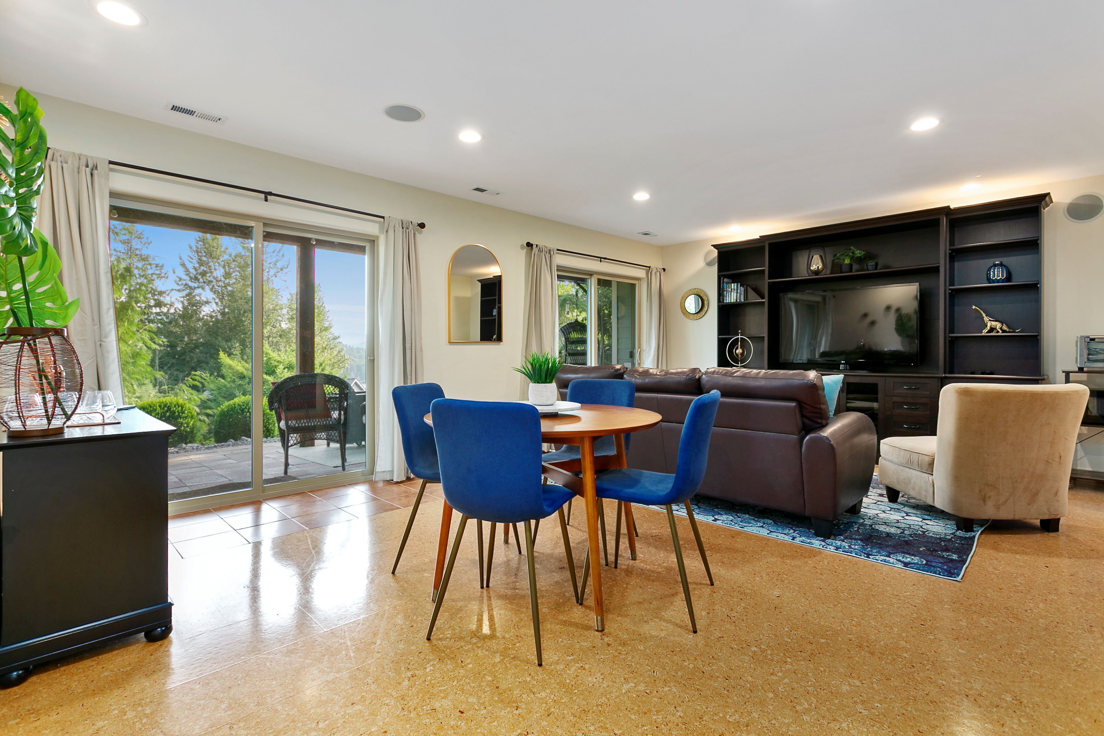 A modern living room with a dining area, large windows, and a flat-screen TV.