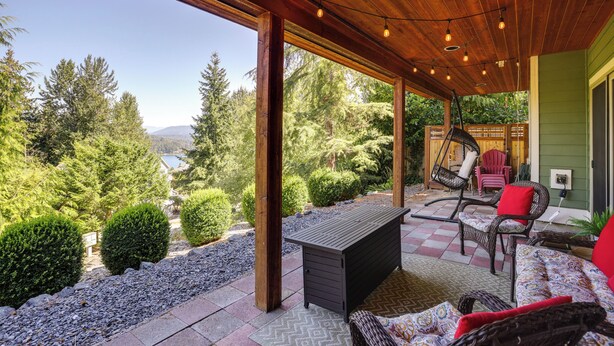 Una veranda riparata con soffitto in legno, una panca, sedie in vimini e vista su una zona boschiva.